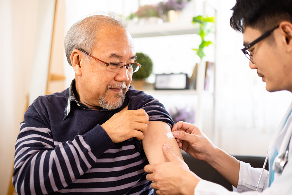 Older Asian male patient receives vaccine from medical provider.